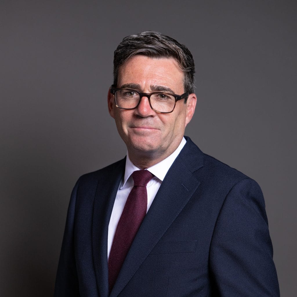 Portrait of a professional businessman wearing glasses and a navy suit with a maroon tie, against a plain grey background.
