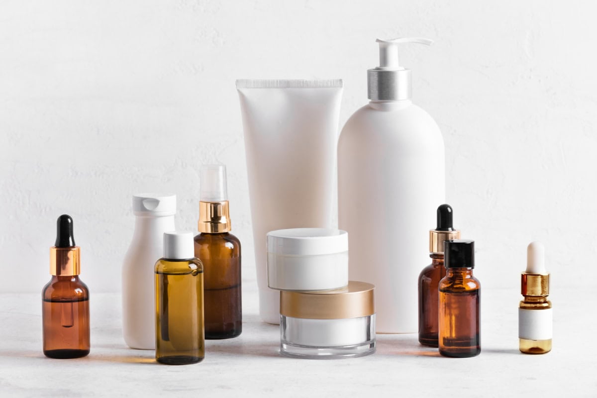 Collection of skincare and beauty products including serums, creams, and oils in amber and white bottles on a white background.