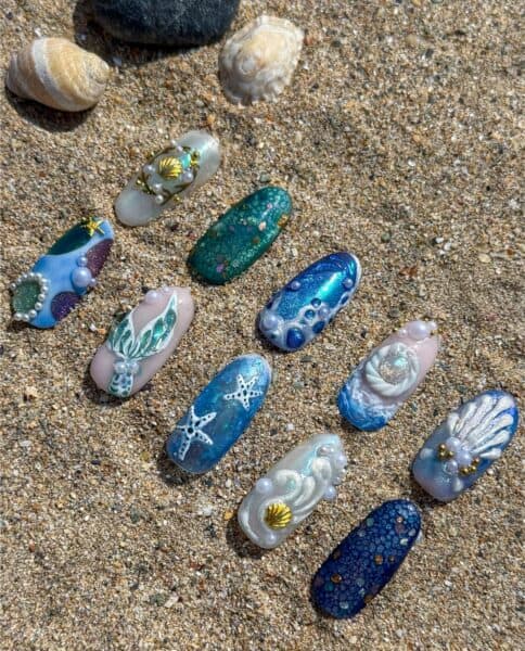 Colorful mermaid-themed nail art designs with shells and starfish on sandy beach surface, perfect for a summer or beach-inspired manicure.