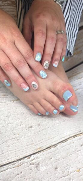 Close-up of hands and feet with light blue and white mermaid-themed nail art, featuring scales and ocean-inspired designs, perfect for a mermaid manicure look.
