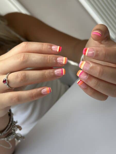 Hands displaying neon striped French tip manicure