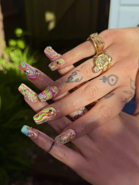 Hands displaying colourful floral nails and gold rings