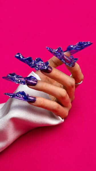 Hand displaying sculptural purple nail art against pink background