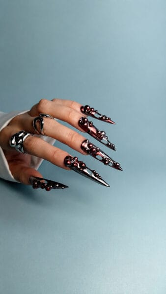 Hand displaying metallic black and burgundy sculptural stiletto nails