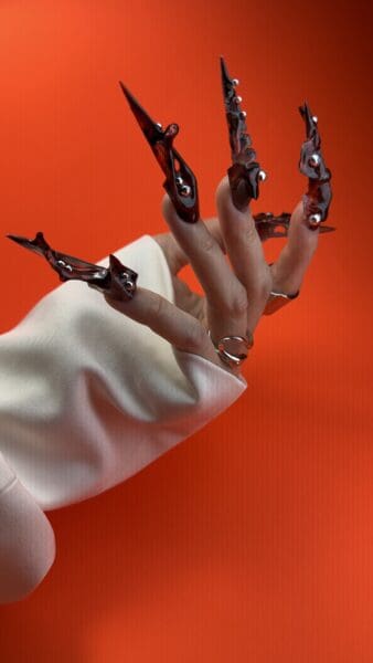 Hand wearing dark sculptural pointed nail art against red background