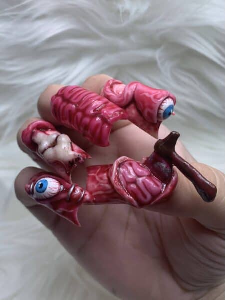 Hand holding grotesque pink eyeball and organ-shaped gummy sweets