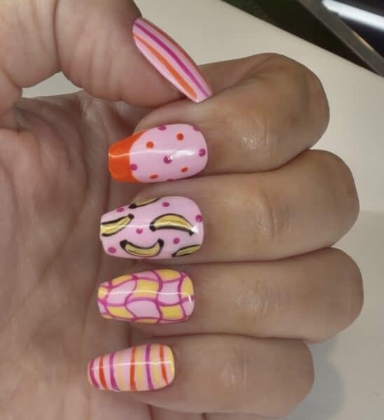 Hand displaying colourful pink fruit-patterned nail art