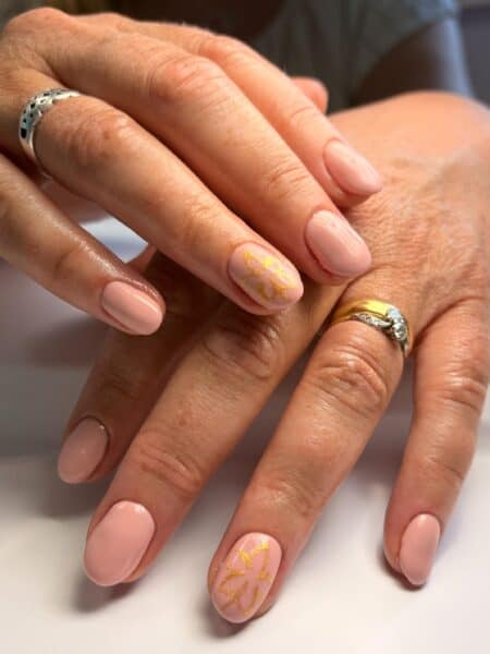 Hands with nude pink nails and gold floral accents