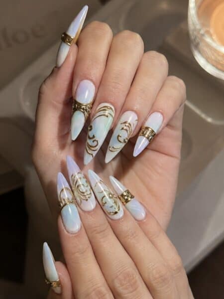 Iridescent stiletto nails with ornate gold embellishments