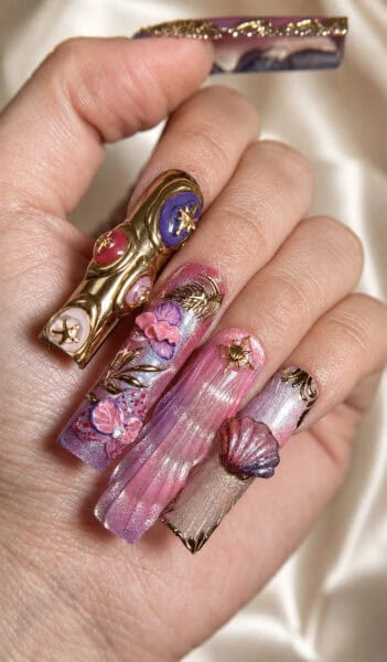 Hand with ornate pink, purple and gold acrylic nail art
