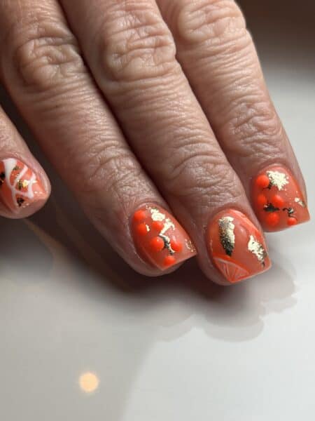 Close-up of orange nails with gold foil decoration