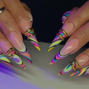 Close-up of long stiletto nails with colourful Pucci-inspired swirl patterns and gold accents, showcasing trendy nail art.
