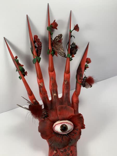 Red clawed hand sculpture with eye and insects