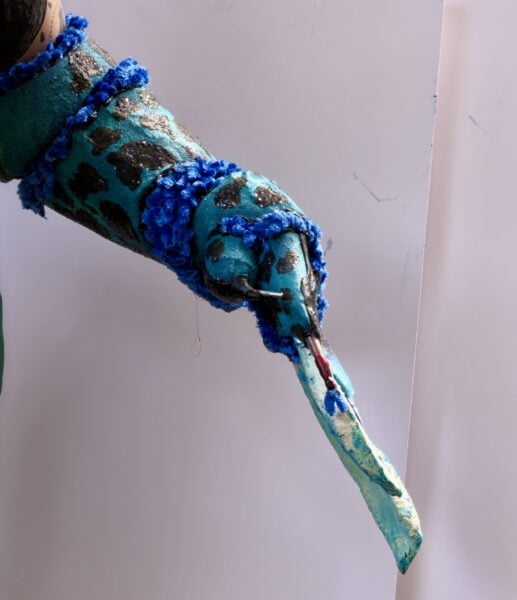 Turquoise painted arm sculpture with blue tassels and metallic accents