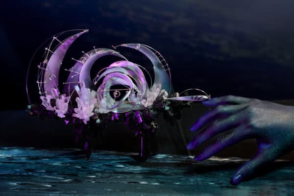 Iridescent gloved hands holding crystal-studded abstract sculpture