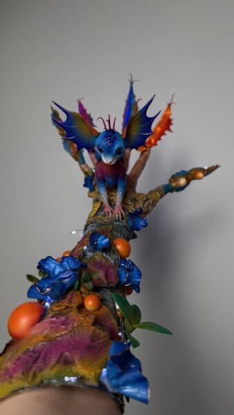Colourful winged fantasy creature sculpture on a branch