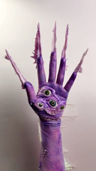 Purple sculptural hand with elongated fingers and embedded eyes