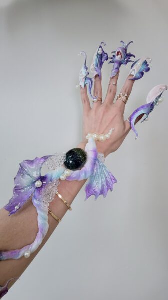 Hand displaying elaborate purple and turquoise fantasy acrylic nails
