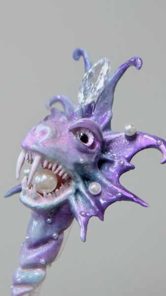 Iridescent purple monster figurine holding a pearl in its mouth