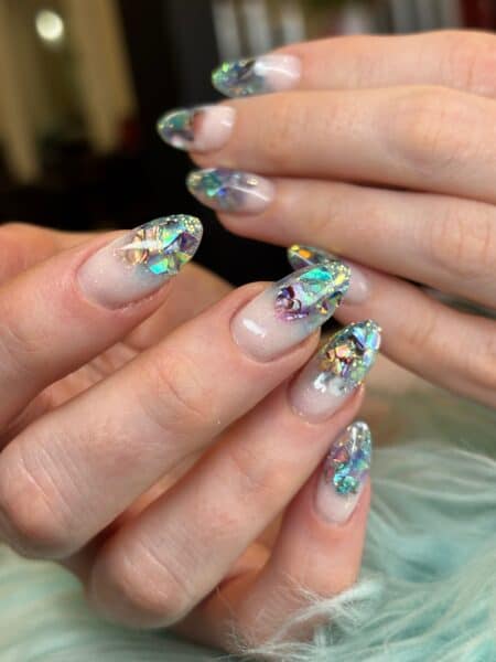 Hands displaying translucent nails with colourful iridescent gem decorations