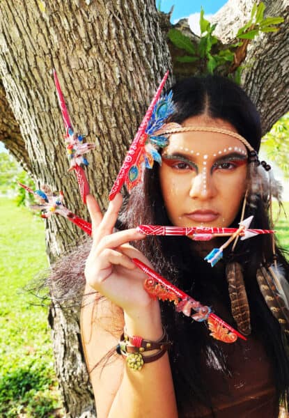 Woman wearing feathered red headdress beside a tree