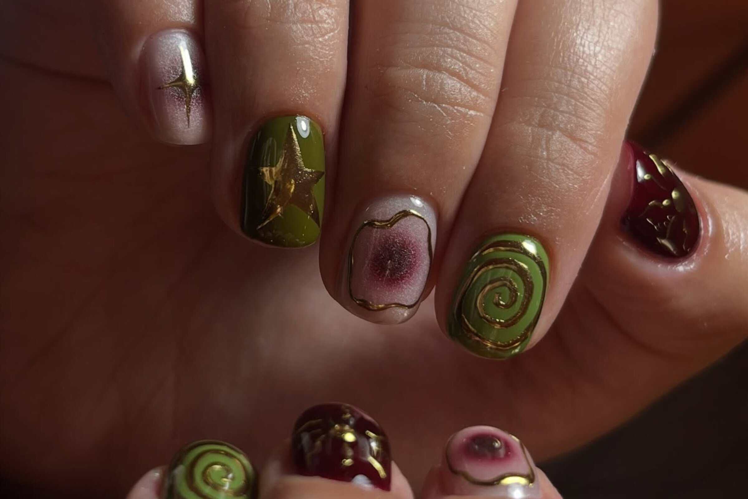 Close-up of glossy green and burgundy swirl nail art