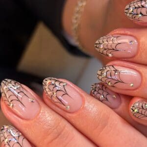 Nude nails with black spiderweb art and rhinestones