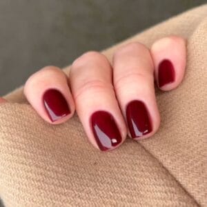 Hand with glossy burgundy nails on beige knit sleeve