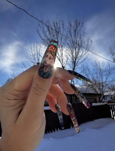 Hand displaying colourful stained-glass portrait nail art outdoors