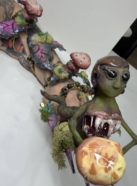 Tattooed hands holding a surreal glazed creature sculpture