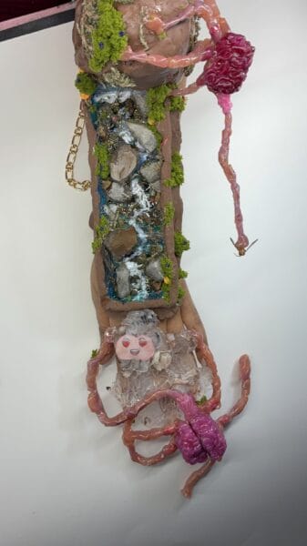 Surreal mixed-media sculpture with waterfall, moss, brains and pink cords.