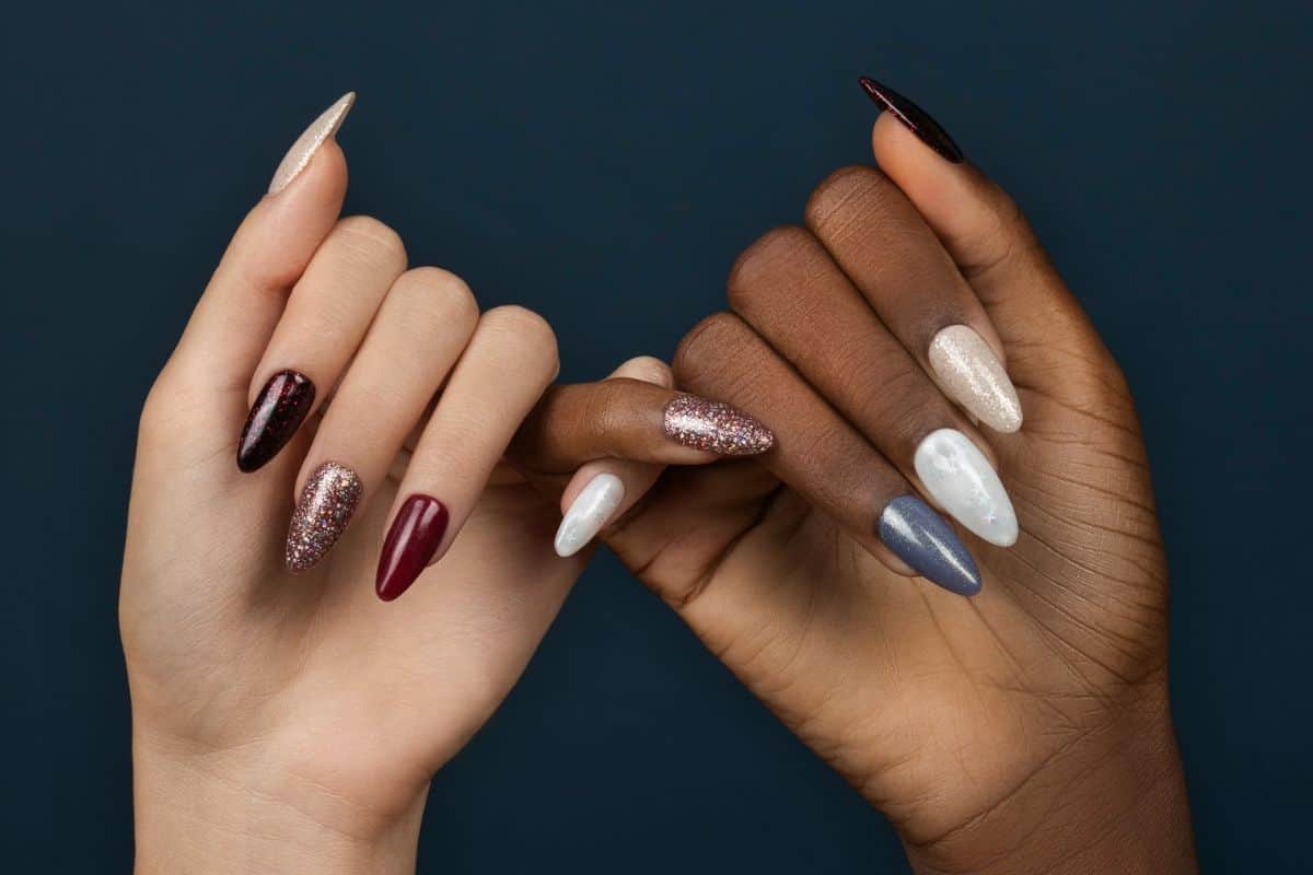 Two hands displaying festive glittered almond-shaped manicures