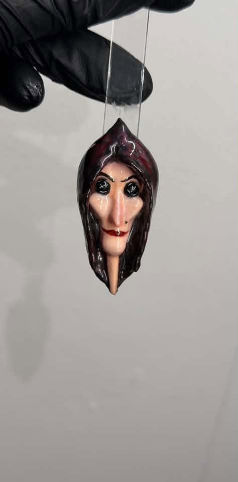 Gloved hand holding a hooded face pendant on clear strip