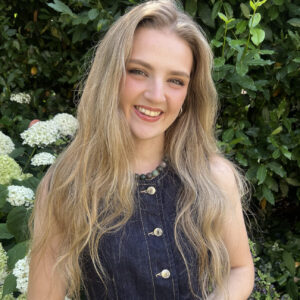 Smiling blonde woman standing beside white garden flowers